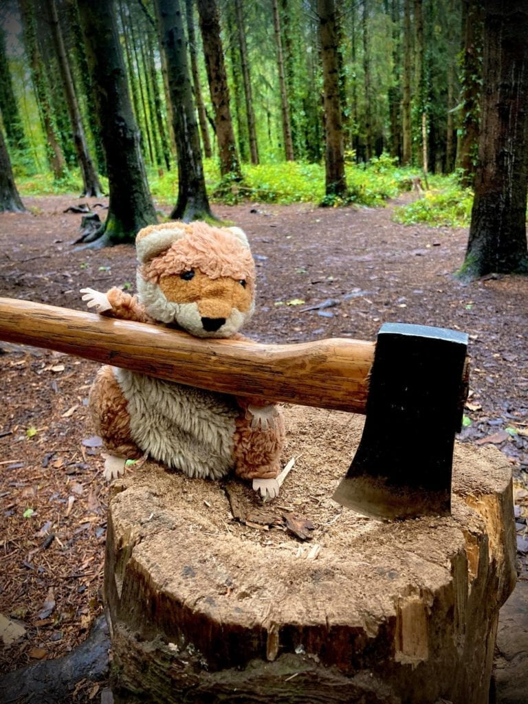 Stuffed-toy-squirrel-posed-to-look-like-chopping-wood-with-axe-on-tree-stump-in-the-woods.