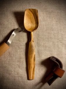 Hook-knife-laying-next-to-wooden-hand-carved-spoon-and-knife-sheath.