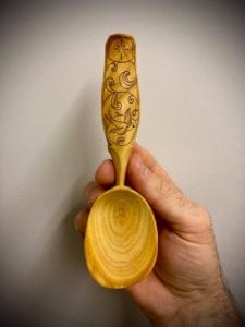 Hand-carved-spoon-being-held-by-hand-against-grey-background.