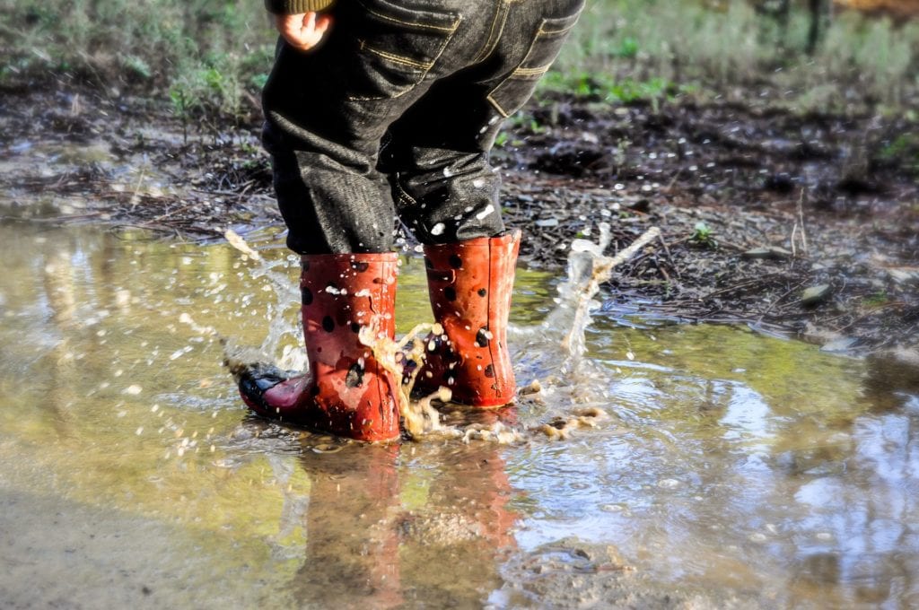 child-splashing-in-muddy-puddle-wearing-red-welly-boots.