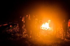 group of people standing around a bonfire at night