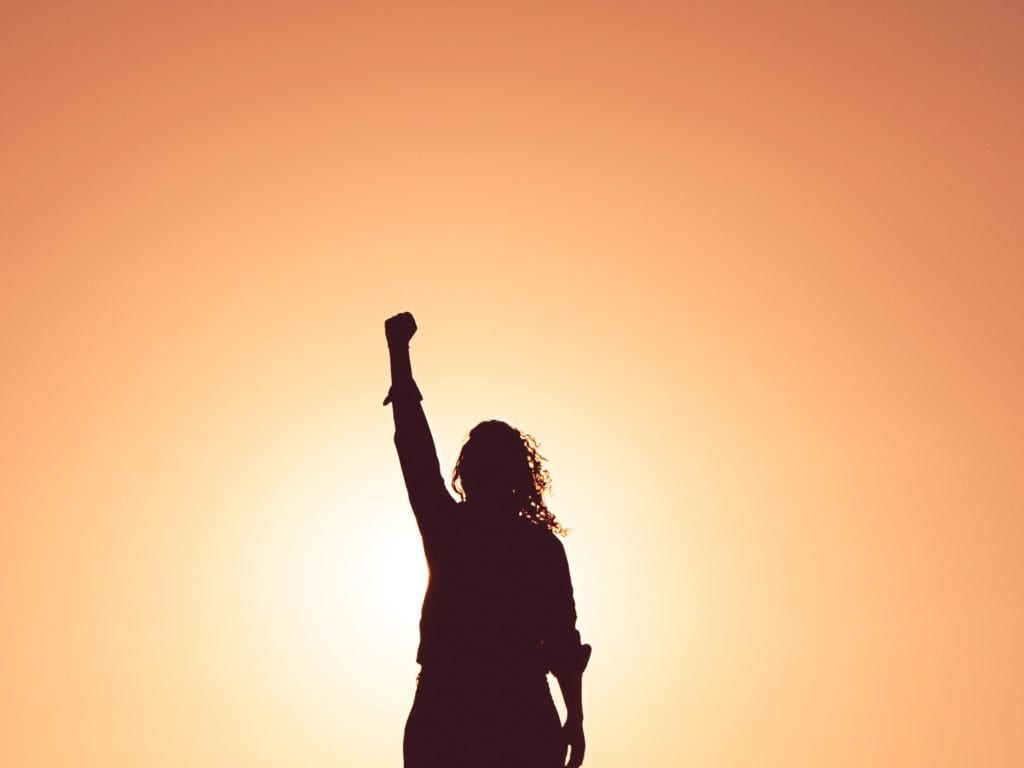 silhouette-of-woman-stood-against-orange-sky-holding-fist-aloft.